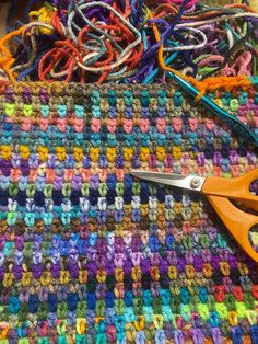 a pair of scissors sitting on top of a multicolored knitted blanket next to yarn