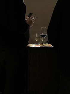 two people standing next to each other looking at cell phones and wine glasses on a table