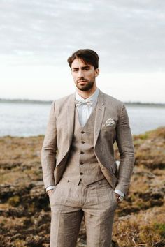 a man in a suit standing next to the ocean with his hands on his hips