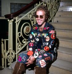 a man sitting on the steps with his shoes covered in patches and badges, smiling at the camera