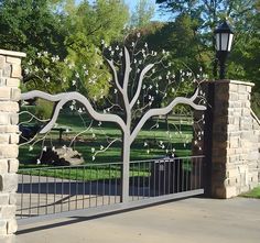 an iron gate with a tree on it in front of a stone wall and street light