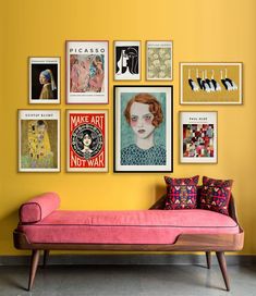 a pink couch sitting in front of a yellow wall with pictures on the wall above it