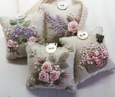 four decorative pillows with flowers on them sitting on a table next to buttons and thread