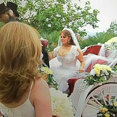 a woman in a wedding dress walking down the street with a horse drawn carriage behind her