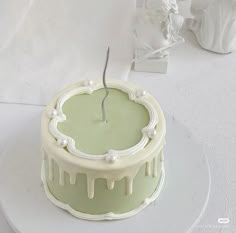 a green and white cake with icing sitting on a plate next to a vase