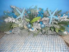 a blue and silver christmas arrangement with snowflakes, evergreens, pine cones, starfish