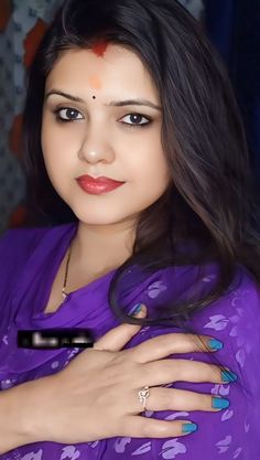 a woman with long dark hair wearing a purple sari and holding her hand on her chest