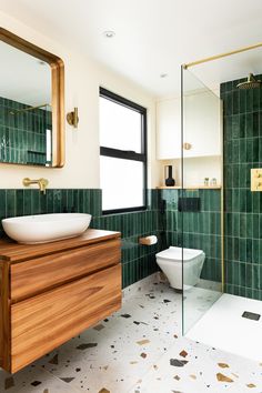 a bathroom with green tile and wooden vanity, mirror, toilet and bathtub in it