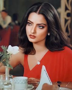 a woman sitting at a table with a white rose in her hand and looking off to the side