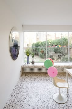 a room with a window, table and chair in it that has balloons on the floor