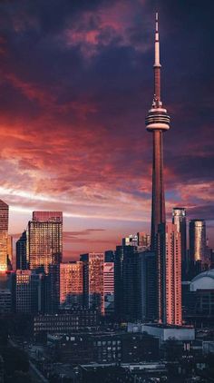 the city skyline is lit up at night with red and purple clouds in the sky