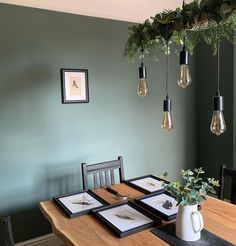 a dining room table with four framed pictures on the wall and hanging lights above it