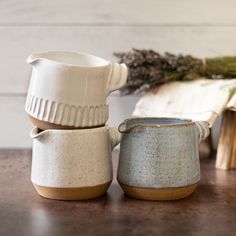 three ceramic cups sitting next to each other on top of a wooden table with dried plants in the background