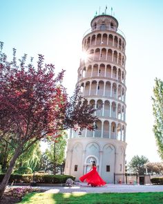 a woman standing in front of a tall tower with a red umbrella on the ground