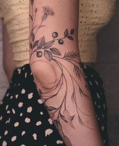 a woman's arm with flowers and leaves tattooed on her left arm, while sitting in a polka dot dress