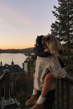 two people hugging each other while standing on a balcony overlooking a lake and houses in the distance