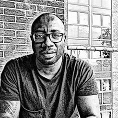 a black and white photo of a man with glasses sitting in front of a brick wall