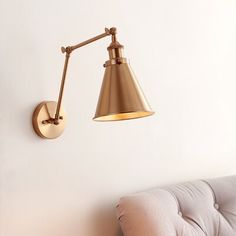 a gold wall light mounted on the side of a white wall next to a couch