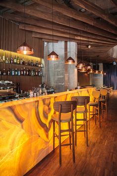 an empty bar with wooden chairs and yellow marble counter top, along with several bottles on the wall