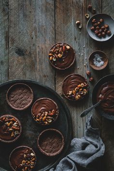 chocolate tart cups with nuts on top and spoons next to them sitting on a wooden table