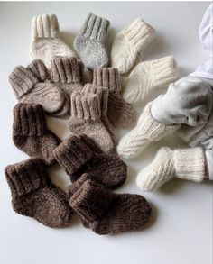 several knitted mittens and gloves laid out on a white surface with one person's hand in the middle