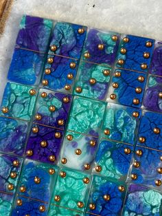 a blue and green tile with gold beads on the bottom is laying on some snow