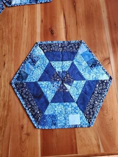 a blue and white patchwork table topper on a wooden floor next to two place mats