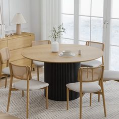 a dining room table with four chairs and a vase on the top, in front of a large window