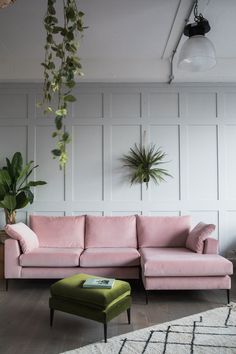 a living room with pink couches and plants on the wall above them, along with a green ottoman