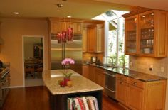 a kitchen with wooden cabinets and marble counter tops, an island in front of the sink