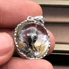 a person holding a glass pendant in their left hand, with the reflection of a tree on it