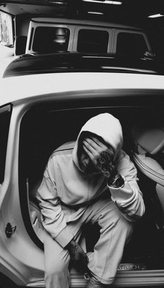 a man sitting in the back of a car looking at his cell phone while wearing a hoodie