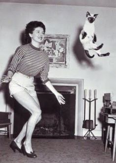 a black and white photo of a woman jumping in the air with a cat above her head