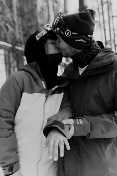 black and white photograph of two people kissing each other in front of snow covered trees