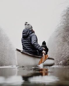 a person in a boat on the water with trees and fog behind them as it is snowing