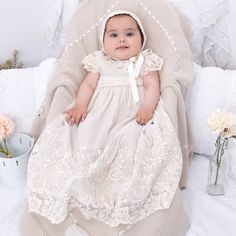 a baby in a white dress sitting on a bed