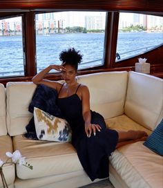 a woman sitting on top of a white couch in front of a window next to a body of water