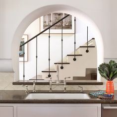 a kitchen counter with a sink under an arched window next to a stair case in the background