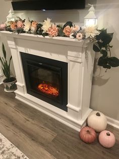 a fireplace with flowers on the mantle and some pumpkins next to it in front of a flat screen tv