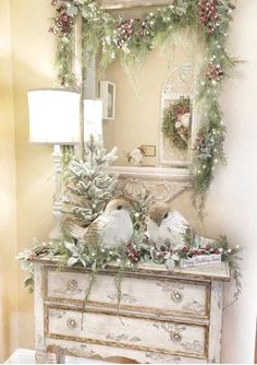 two birds sitting on top of a dresser next to a mirror and christmas wreaths