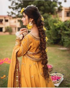 a woman with long hair wearing a yellow dress and flower in her hair, standing outside