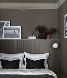 a bed with white sheets and black pillows in a bedroom next to pictures on the wall