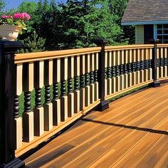 a wooden deck with black railing and flower pot on it's end, in front of a house