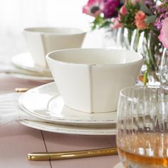 a table set for two with flowers in vases and wine glasses on the side