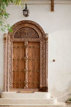 an ornate wooden door in front of a white wall with plants growing on the steps