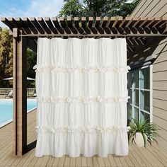 a white curtain hanging from the side of a wooden pergole over a pool