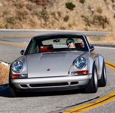 a man driving a silver sports car down a curvy road