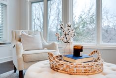 a living room with a couch, chair and book on the coffee table in front of large windows