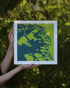 a person holding up a green and blue print in front of some trees with leaves