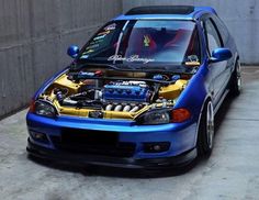 a blue car parked in front of a building with its hood up and engine bay open